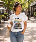Smiling woman on a sunny street wearing a white T-shirt that reads 'BRB... Aligning My Chakras,' holding an iced coffee.