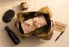 Custom-gift-hamper-with-printed-apparel,-dark-gold-tissue-paper-and-kraft-ribbon-on-a-cream-linen-surface